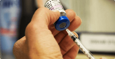 A hand holding a syringe and a vaccine