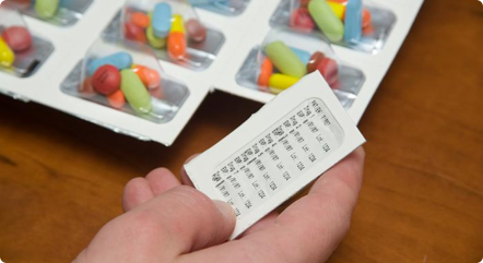A hand holding a note with medicine tablets in the background
